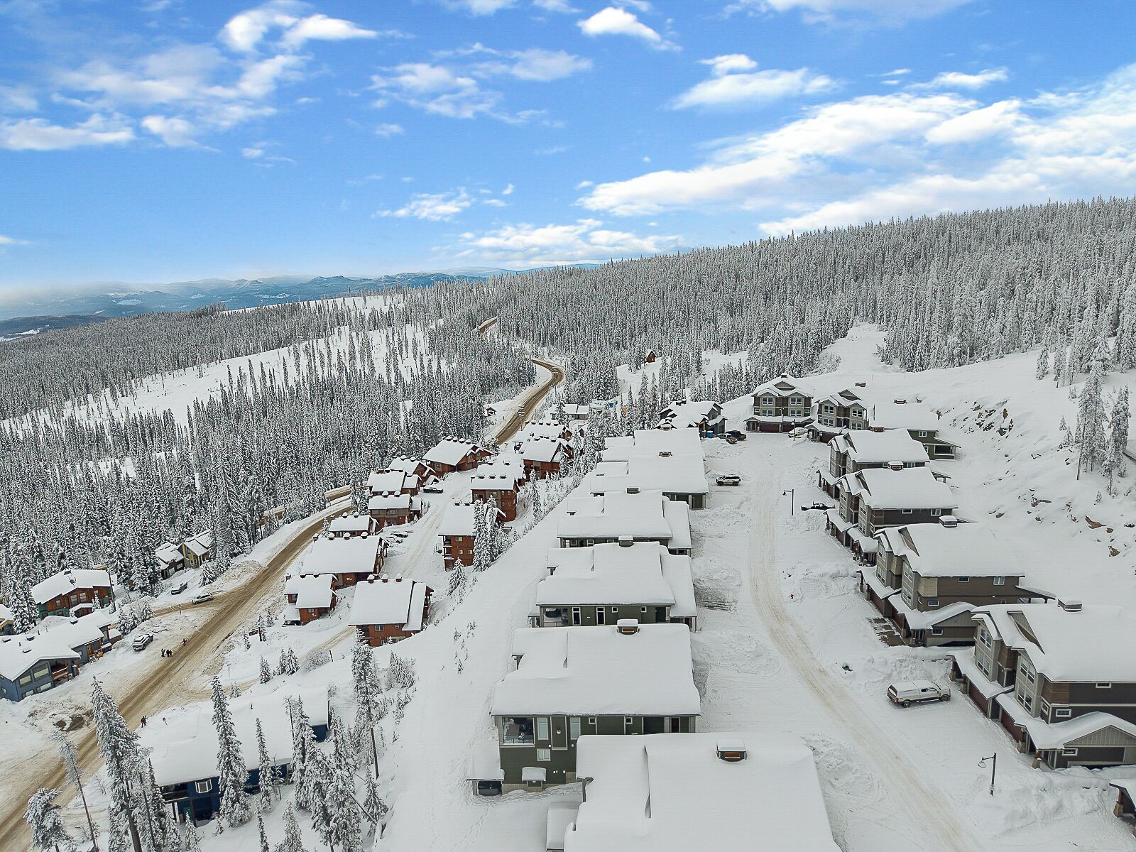 Estância de esqui coberta de neve, com vários edifícios, uma pista de esqui e uma floresta densa ao fundo.