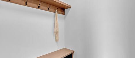 A corner of a room with a wooden shelf, a coat rack, and a bench.