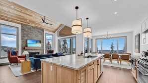 A spacious kitchen with a large island, wooden cabinets, and a view of snowy trees. - Western Star Chalet Ski In Out w Mtn View (Beaverdell)