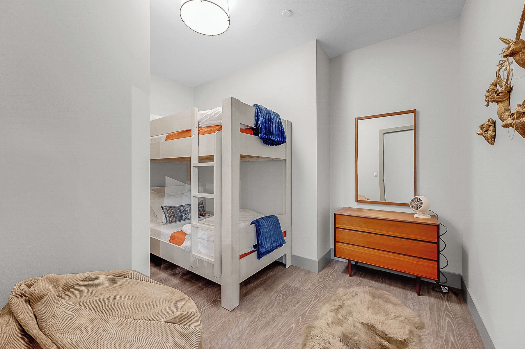 Una cama individual con espejo y cómoda, un sillón redondo y una alfombra mullida en una habitación con suelo de madera.