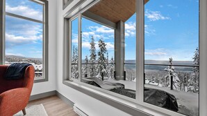 A room with large windows, a red chair, and a view of snow-covered trees. - Western Star Chalet Ski In Out w Mtn View (Beaverdell)
