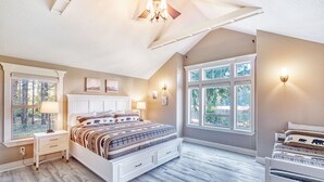 A bedroom with a large bed, two bedside tables, a ceiling fan, and a window with a view of trees. - Private Lake, Amazing View, Hot Tub, Forest Trail (Long Beach)