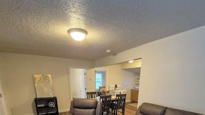 A living room with a brown leather sofa, a matching armchair, and a patterned rug. There is a dining area with a table and chairs in the background.
