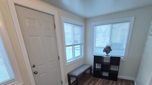 A room with a wooden floor, a bench, a door, and two windows with blinds.