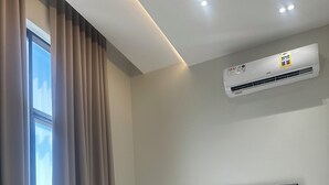 Una camera da letto moderna con un letto imbottito grigio, biancheria beige e un'ampia finestra con tende.