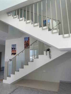 A modern staircase with glass railings and a white interior. - Gorgeous 4-bedroom Chalet with Pool in peaceful Rumais (ابوالنخيل)