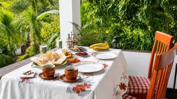 A table set outdoors with a white tablecloth, plates, cups, and food items.