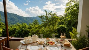 A table set for a meal with tea service, plates, and glasses, overlooking a mountainous landscape. - Hilltop Retreat Matale (Walewela)