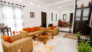 A living room with striped sofas, a wooden coffee table, and a dining area in the background. - Hilltop Retreat Matale (Walewela)
