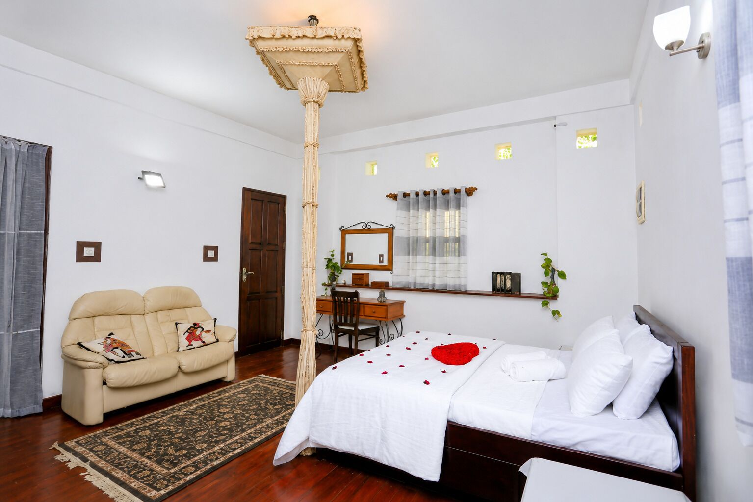 A bedroom with a bed, a desk, a chair, a sofa, and a large pillar.