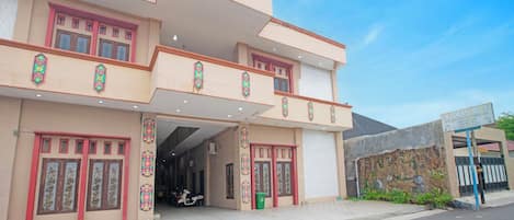 A multi-story building with a covered entrance, decorative window frames, and a green trash bin.