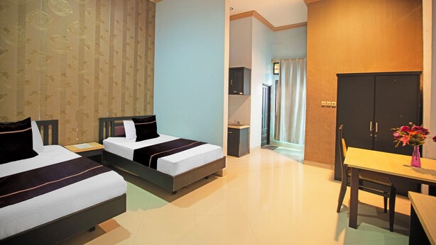 Ein Hotelzimmer mit zwei Betten, einem Holzschrank, einem kleinen Tisch mit einer Vase und einem durch eine Tür erreichbaren Badezimmer.