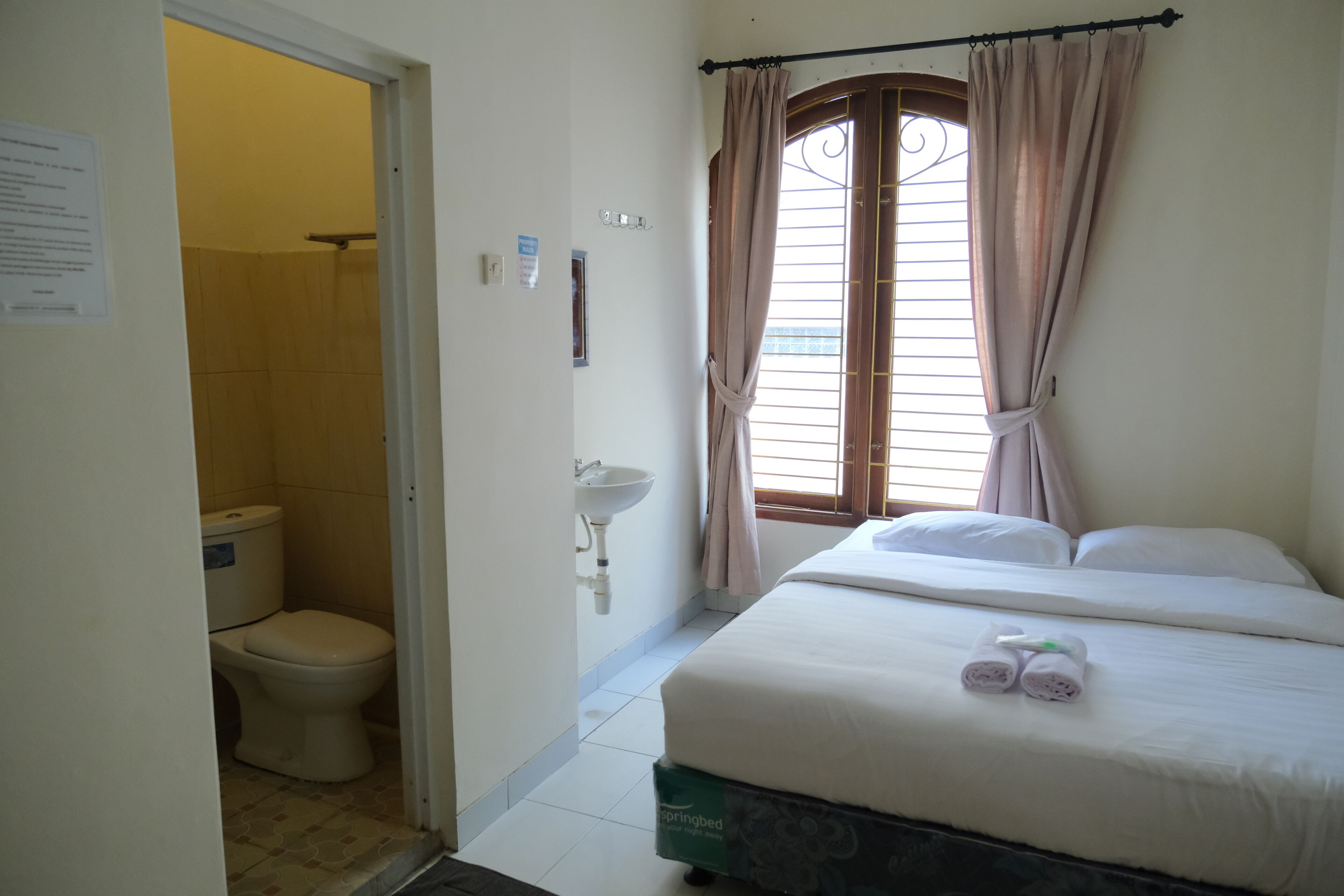 A bedroom with a bed, a window with curtains, a sink, and a toilet.