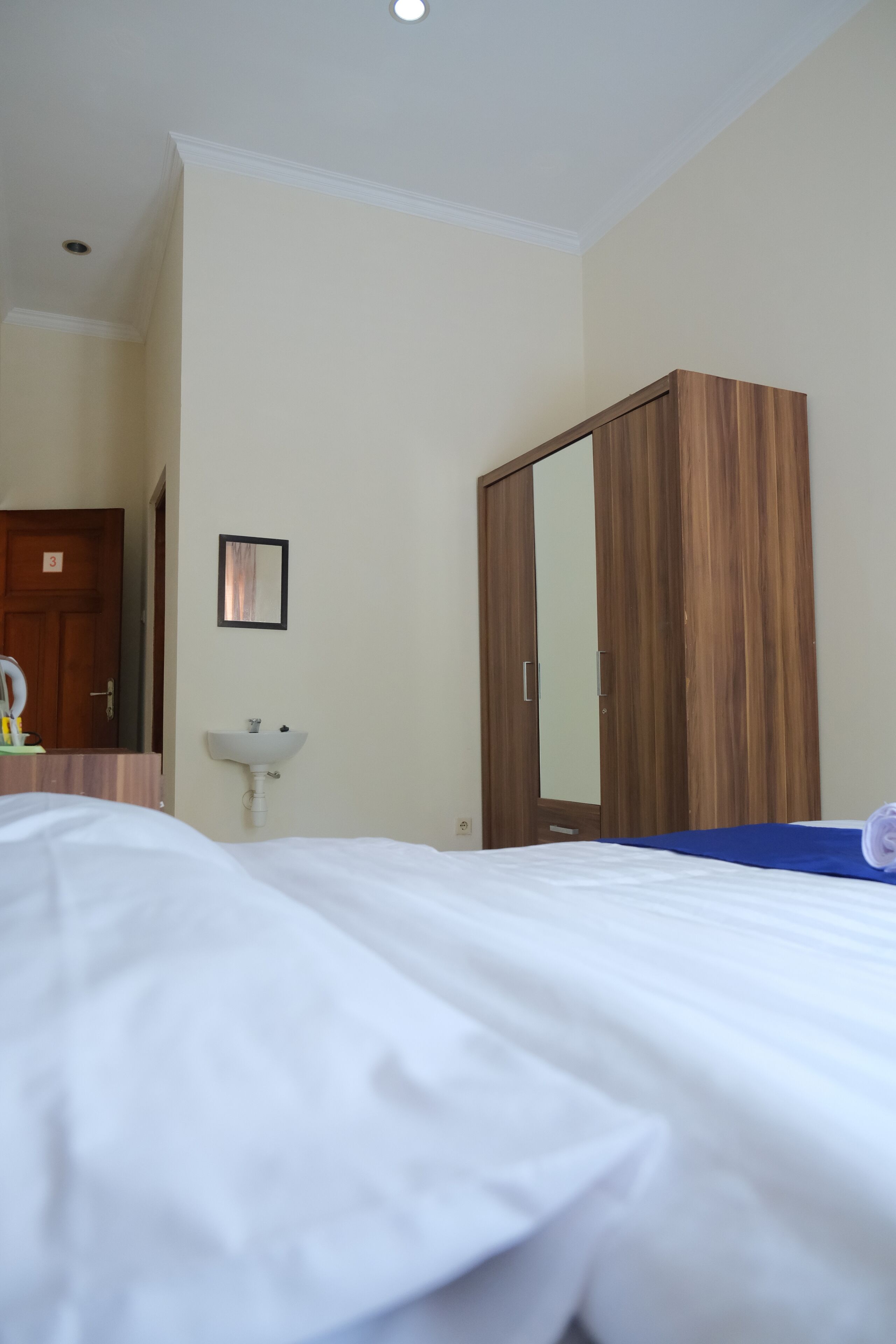Une chambre d’hôtel avec un lit, une armoire en bois, un lavabo et un miroir.