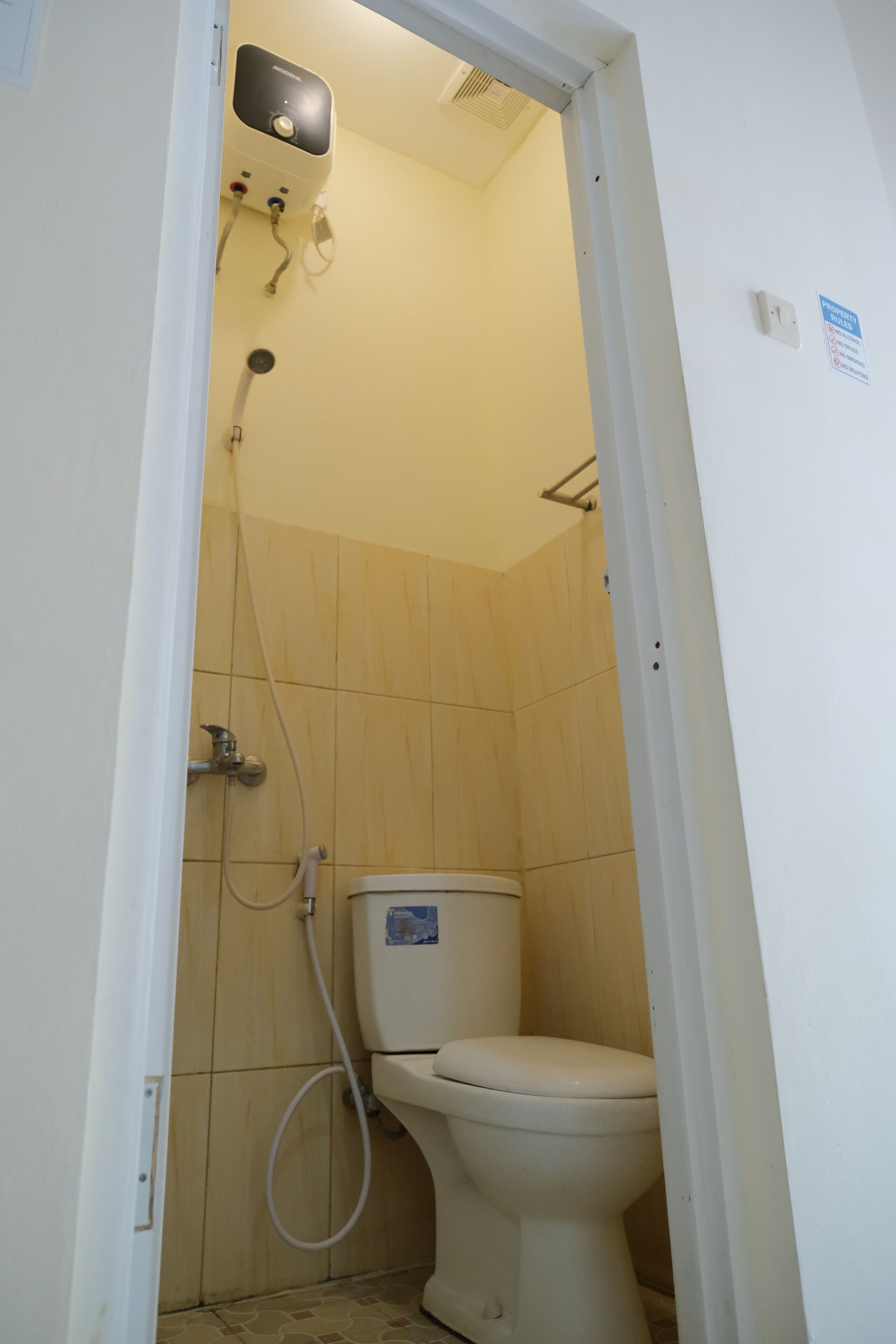 A small, enclosed bathroom with a toilet, a shower, and a wall-mounted heater.