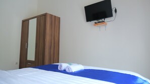 Una habitación de hotel con cama, televisor montado en la pared y un armario de madera.