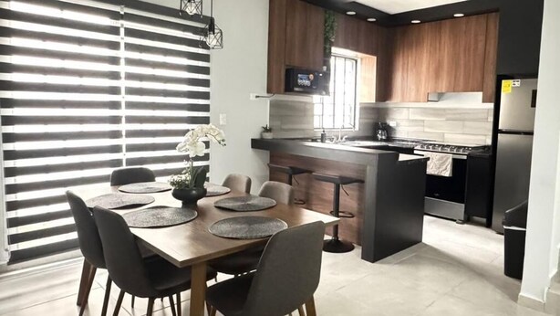Una cocina moderna con una isla central, armarios oscuros y una zona de comedor con mesa y sillas de madera.