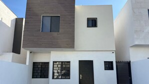 Un edificio moderno de dos pisos con techo plano, una puerta central y una pequeña ventana en el piso superior.