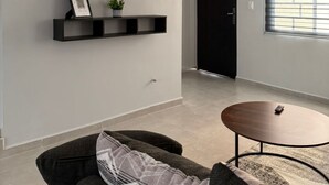 Una sala moderna con un televisor de pantalla plana montado en la pared, un ventilador de techo, una puerta negra y una ventana con persianas.