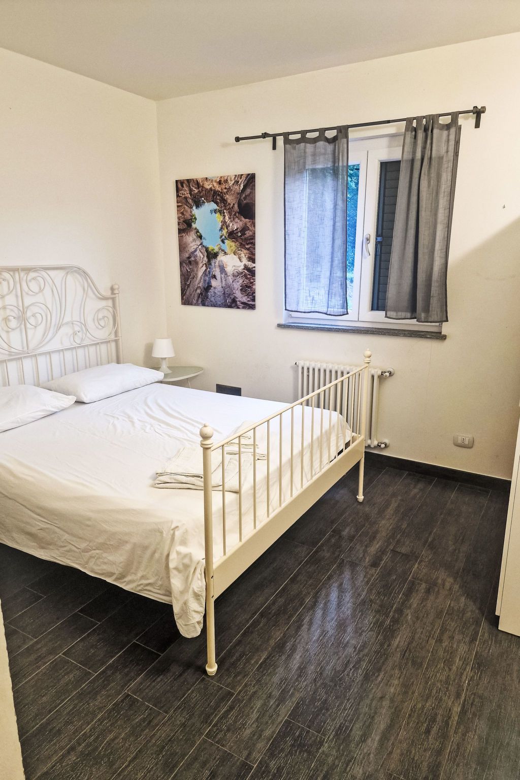 Une chambre avec un lit simple, une fenêtre avec des rideaux, un radiateur et une œuvre d’art accrochée au mur.