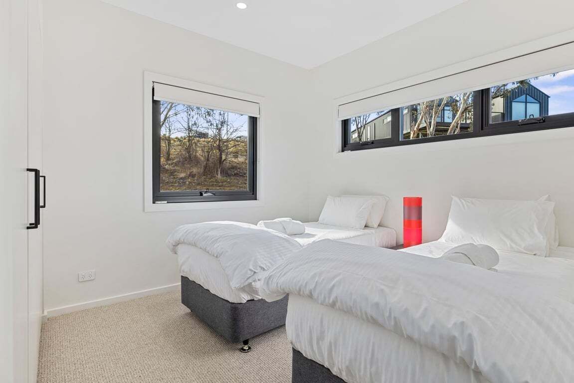 A modern bedroom with two beds, a large window, and a view of the outdoors.