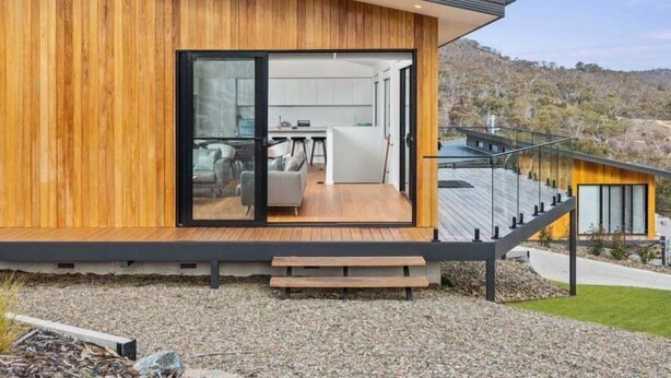 Una casa moderna con fachada de madera, un vidrio que da a una sala de estar y vistas del paisaje circundante.