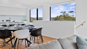 Una cocina moderna con armarios blancos, una mesa de comedor dispuesta para cuatro personas y ventanas amplias con vistas al campo.