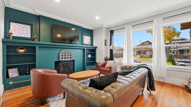 A living room with teal walls, a fireplace, a leather sofa, and a large window with a view of houses. - Newly renovated 2-bedroom apartment in quiet Historic Detroit neighborhood (Detroit)