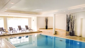 Et indendørs swimmingpool med krystalklart vand, omgivet af liggestole og plantekrukker.