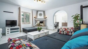 Ein modernes Wohnzimmer mit Sofa, Fernseher, Kamin und einem Essbereich, der durch einen Bogen sichtbar ist.