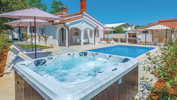 Ein Poolbereich mit Whirlpool, Liegestühlen und Sonnenschirmen.
