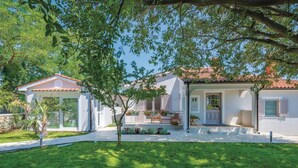 Ein zweistöckiges Haus mit einer überdachten Terrasse und einem kleinen Garten.