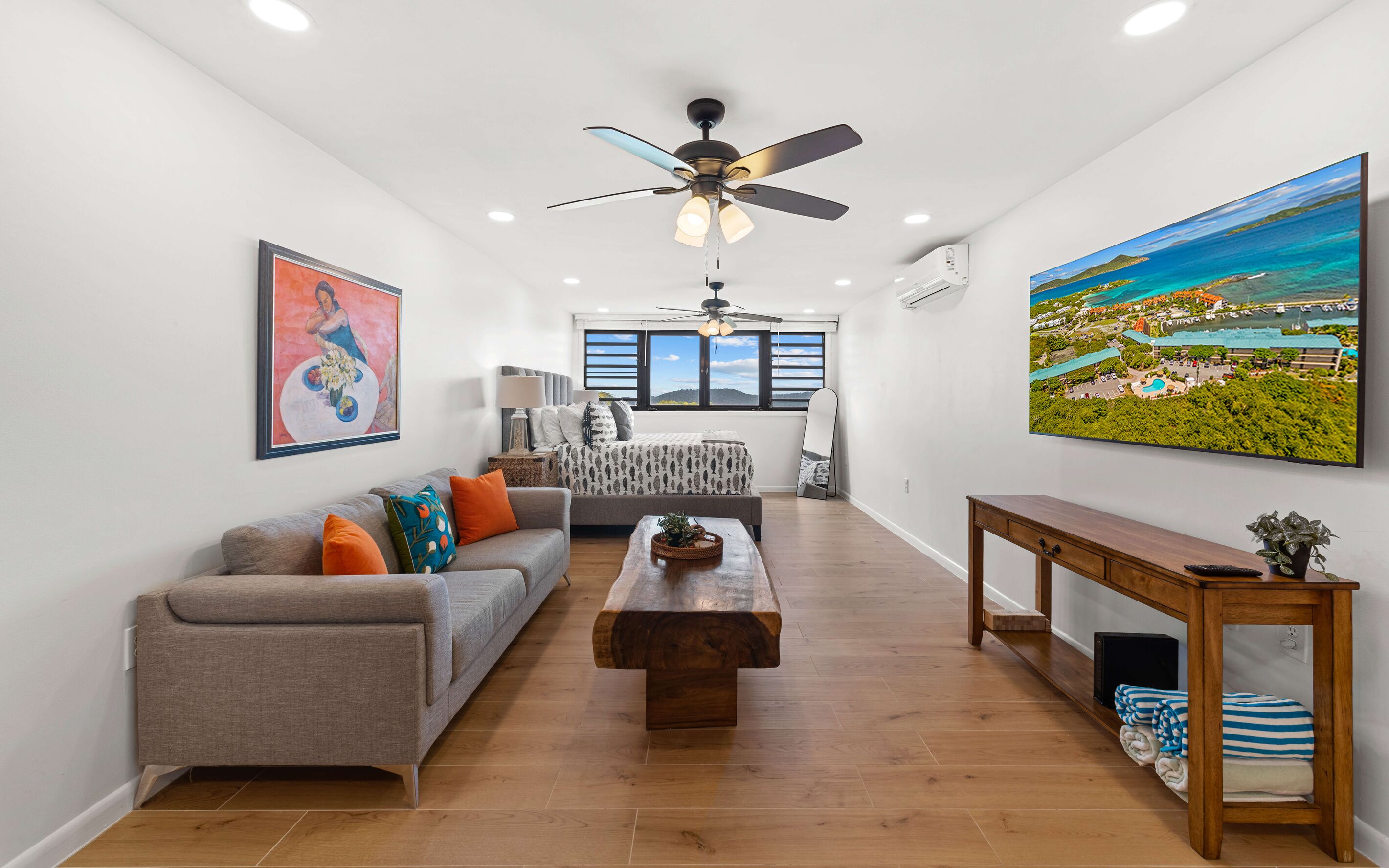 A modern living room with a sofa, coffee table, and a painting of a tropical landscape.