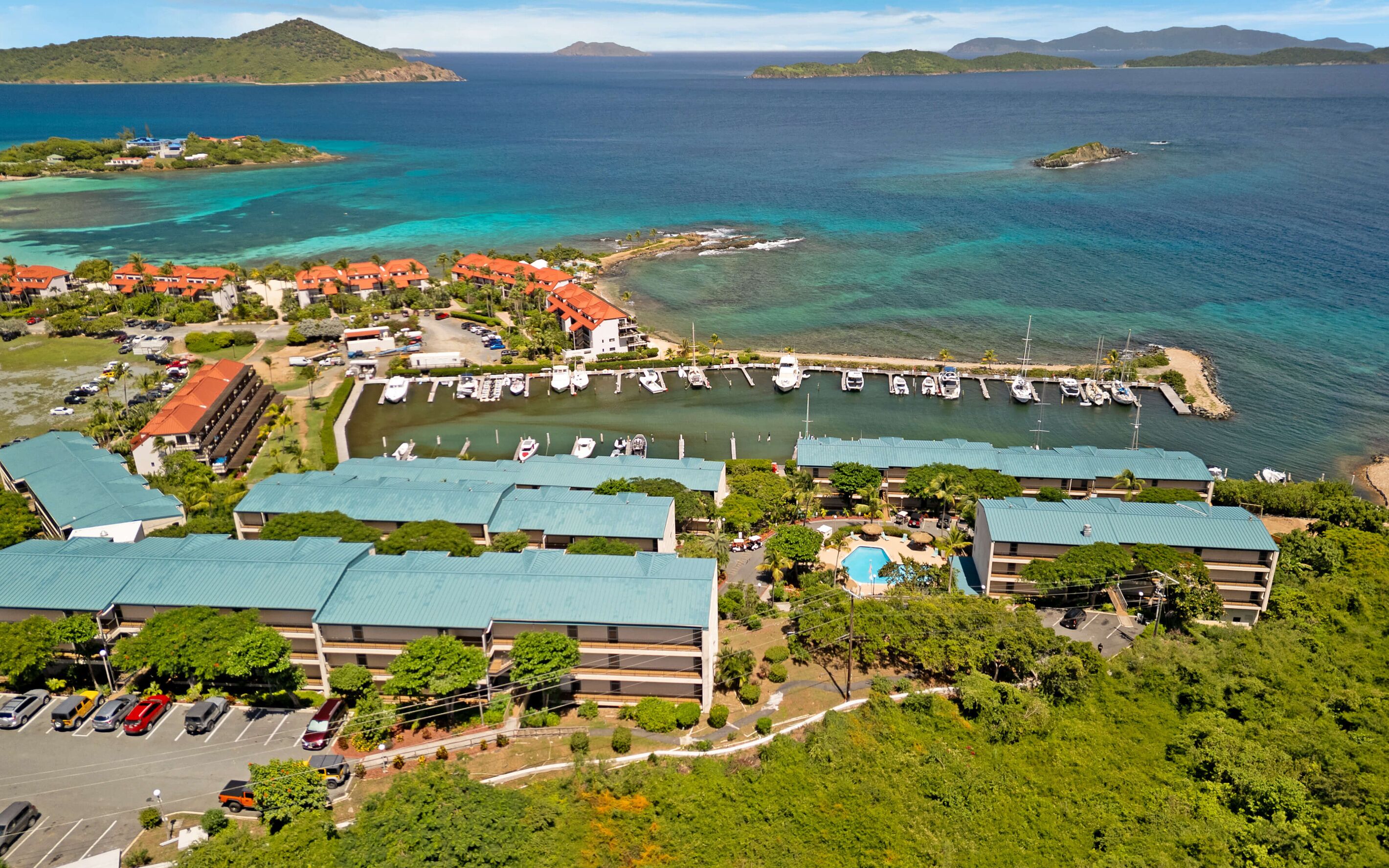 An aerial view of a coastal resort with multiple buildings, a marina, and clear blue waters.