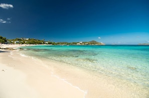 A beach with clear turquoise water, sandy shore, and buildings in the background. - 2 Pools, Dining | Walk to Beach | Sapphire Village (St. Thomas)