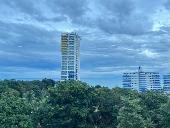Un hotel alto con varios pisos y balcones, rodeado de abundante follaje verde y un cielo nublado.