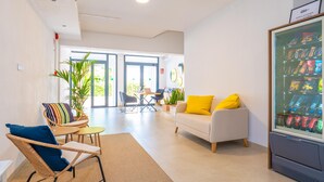 Un intérieur moderne avec un canapé, des fauteuils, une petite table, une plante et un distributeur automatique.