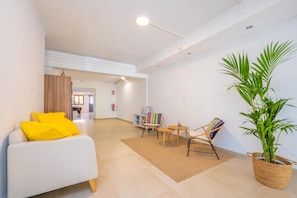 Un espace de vie moderne avec un canapé blanc, une petite table ronde, deux chaises, une bibliothèque et une grande plante en pot.