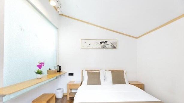 A bedroom with a bed, bedside tables, a nightstand, a small shelf with a plant, and a framed picture on the wall. - Tuoshui Ballad Courtyard Boutique Inn (Fenghuang)
