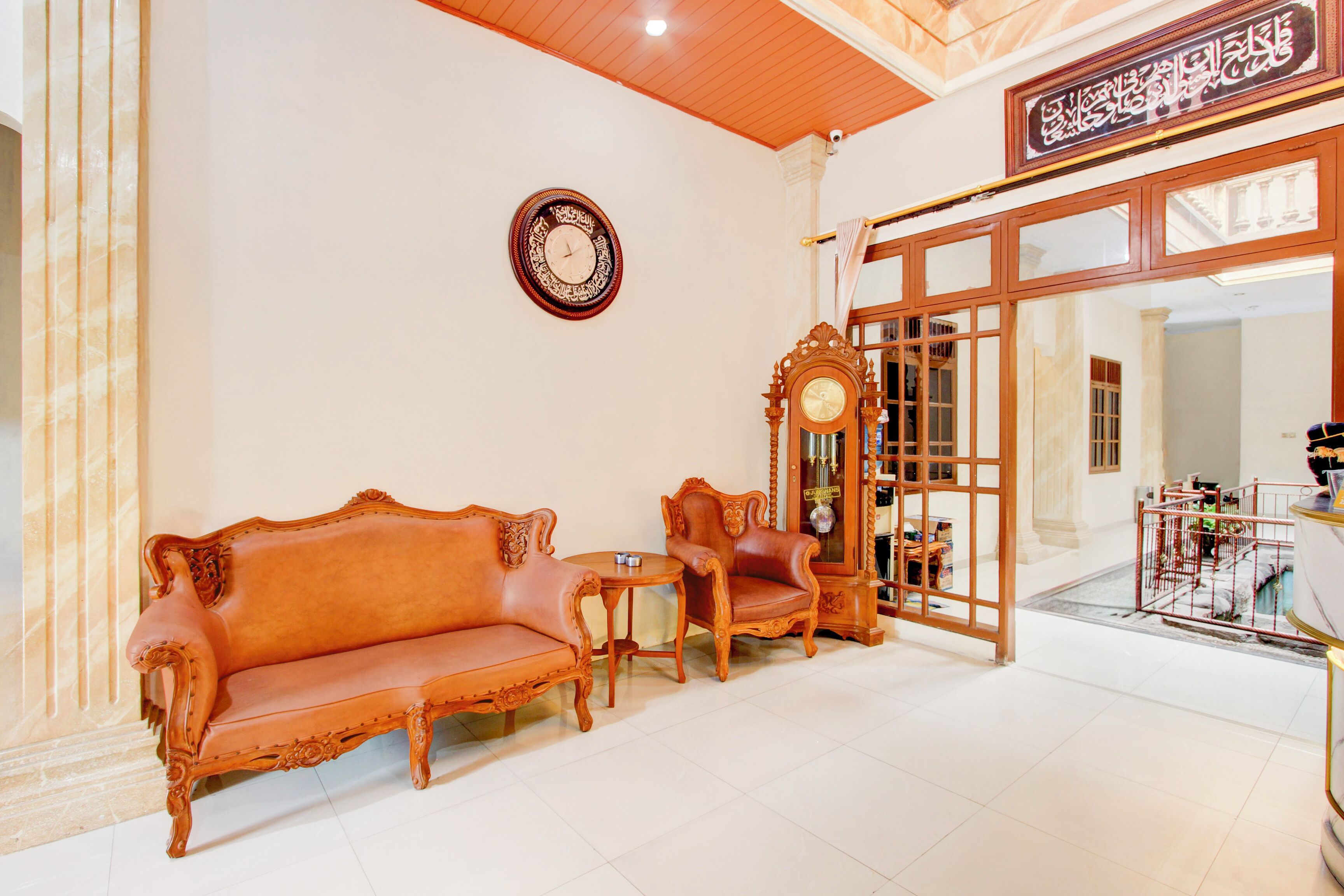 A room with a sofa, armchair, and a small table. There is a wall clock and a large wooden door with glass panels.