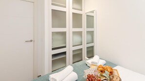 A hotel room with a large closet, a bed with a blue blanket, and a tray with towels, grapes, and a glass. - Apartment + Workspace Chamberí (Madrid)