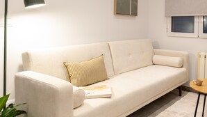 A beige sofa with a cushion, a small table with a cup, and a potted plant. - Apartment + Workspace Chamberí (Madrid)