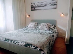 Un lit avec une literie à motifs, une tête de lit et deux lampes fixées au mur.