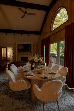 A dining room with a round table set for six, white chairs, a vase of flowers, and a lit candle. - Wellness Escape I Sauna, Hot Tub, Theater & Game Room (East Stroudsburg)