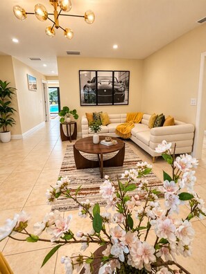 A spacious living room with a beige sofa, a coffee table, and a large painting on the wall. - Moon Luxury Retreat/Heated Pool (Sarasota)
