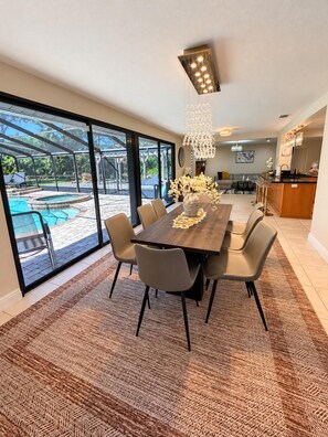 A modern dining area with a large table, chairs, and a view of an outdoor pool. - Moon Luxury Retreat/Heated Pool (Sarasota)
