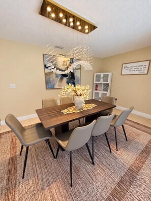 Un coin repas avec une table en bois, quatre chaises, un vase de fleurs et un tableau accroché au mur.