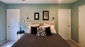 A bedroom with a bed, a ceiling fan, two framed artworks, and a bedside lamp. - Omiha Exclusive Retreat (Waiheke Island)