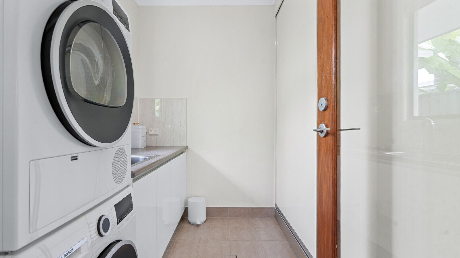 Un cuarto de lavado con lavadoras apiladas, un lavamanos y una puerta a un dormitorio.