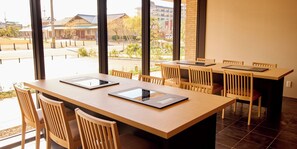 A modern dining area with a long table, several chairs, and large windows offering a view of the street and buildings outside.